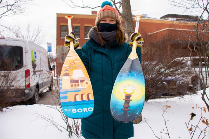 Dawn Pond, Downtown Vibrancy Manager of the Peterborough Downtown Business Improvement Area, displays two of the 20 paddles painted by volunteer community artists to raise funds for the One City Employment Program, which provides meaningful work to those with barriers to traditional employment. The paddles will be on display in the Commerce Building in downtown Peterborough as part of the First Friday Peterborough art crawl. (Photo courtesy of Peterborough DBIA)