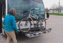 Susan Sauve, transportation demand management planner with the City of Peterborough, demonstrates unloading a bike from a bicycle rack on the front of a Peterborugh Transit bus. The bike racks are part of a pilot program and are available on a limited number of buses on Routes 4, 5, and 8. (YouTube screenshot)