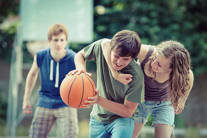 Three teens playing street basketball. (Stock photo)