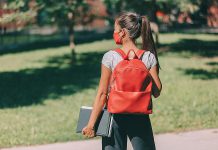 A young masked female student wearing a backpack and carrying books. (Stock photo)