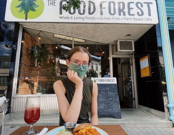Brianna Wood, sister of The Food Forest's owner Lasair Wood, sits at the single-table patio in front of the vegan restaurant. Thanks to a proposal by landlord Ashburnham Realty, The Food Forest has an additional four tables on a back patio shared with Providence and St Veronus. (Photo: The Food Forest / Facebook)