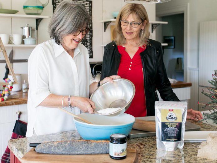 South Pond Farms owner Danielle French in the kitchen with her friend Leslie Scott, owner of Walton Wood Farm. Scott, who primarily sells her brand of personal self-care products as well as some food products (such as the garlic and parmesan beer bread mix pictured) has expanded Walton Wood Farm's product line to include South Pond Farms' gourmet food products, which include jams, marmalade, honey, sauces, baking mixes, and more. (Photo: Ash Nayler Photography)  