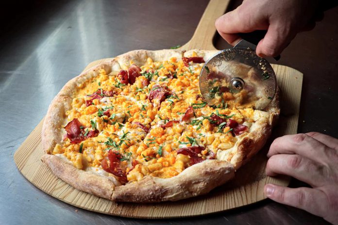 Pizza Bodega, one of 18 downtown Peterborough restaurants participating in the first-ever Mac + Cheese Festival during the month of October, is offering a New York style thin crust "Mac n Cheeza" with a homemade mac and cheese sauce, double smoked spicy capicola ham, fior di latte, parmesan roasted garlic crema, and a sprinkle of cheddar cheese topped with a Cheetos crumble.  (Photo: Mac + Cheese Festival / Peterborough DBIA)