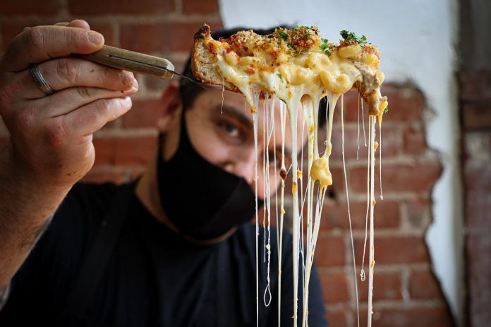 Taso Hatzianastasiou, owner and chef of Taso's Restaurant and Pizzeria, shows off his Chicago-style deep dish "Mac n Cheeza" with spicy chorizo sausage, porchetta, and jalapeno, topped with three cheeses and a garlic parm crusted panko. (Photo: Mac + Cheese Festival / Peterborough DBIA)
