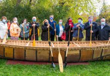 Speakers at The Canadian Canoe Museum's construction commencement event on October 16, 2021 in front of a 26-foot long birchbark canoe built by Métis elder Marcel Labelle: Chief Laurie Carr, Janet McCue, Chief Emily Whetung, Marcel Labelle, Minister Lisa MacLeod, MPP Dave Smith, Carolyn Hyslop, Victoria Grant, Jeremy Ward, Warden J. Murray Jones, and Councilor Andy Dufrane. (Photo: FusionRiver Photography courtesy of The Canadian Canoe Museum)