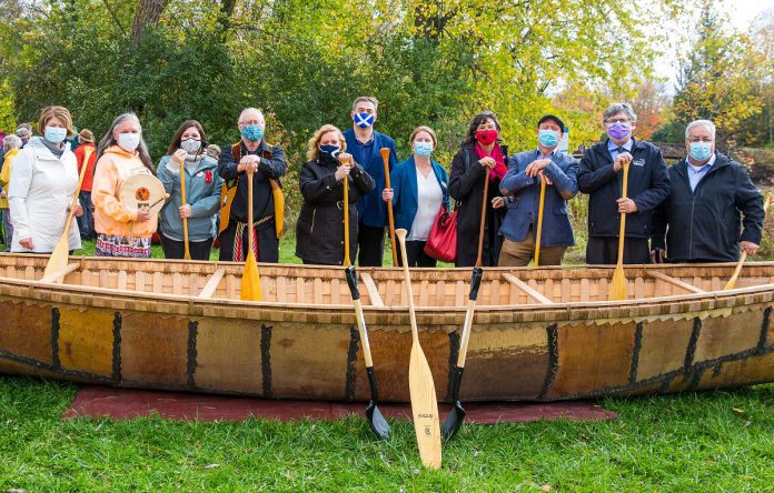 Speakers at The Canadian Canoe Museum's construction commencement event on October 16, 2021 in front of a 26-foot long birchbark canoe built by Métis elder Marcel Labelle: Chief Laurie Carr, Janet McCue, Chief Emily Whetung, Marcel Labelle, Minister Lisa MacLeod, MPP Dave Smith, Carolyn Hyslop, Victoria Grant, Jeremy Ward, Warden J. Murray Jones, and Councilor Andy Dufrane. (Photo: FusionRiver Photography courtesy of The Canadian Canoe Museum)
