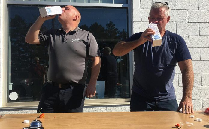 Mark Smith, operations manager of  Fitzsimmons Towing and Repair in Peterborough, and retired Peterborough OPP constable Dave McNabb guzzle milk donated by Kawartha Dairy after eating a ghost pepper in a fundraising event on October 19, 2021 for One City Peterborough. (Photo: Paul Rellinger / kawarthaNOW)