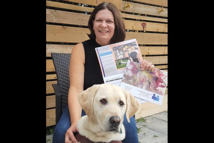 Leslie Yee, chair of the Canadian Council of the Blind's Peterborough chapter, with her guide dog Akira, displays the organization's 2022 fundraising calendar featuring cover art by Peterborough artist Lynda Todd. (Supplied photo)