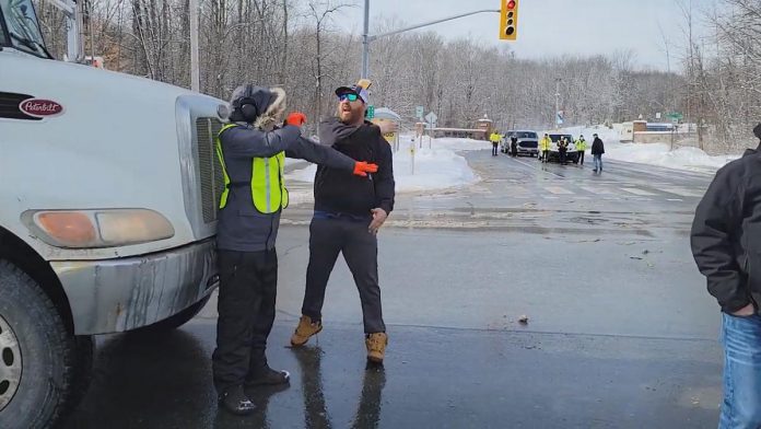 A convoy participant slaps away the hand of a counter-protester who was blocking a dump truck from proceeding through the intersection at Brealey Drive and Stenson Boulevard in Peterborough on February 19, 2022. The counter-protester was arrested and charged under the criminal code with intimidation for blocking the highway, and the convoy participant was arrested and charged with assault. (kawarthaNOW screenshot)