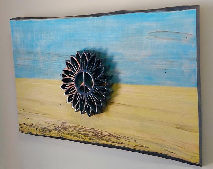 "Rise Above" (21.5" x 13.5") by Peterborough artist Nick Leniuk features a hand-carved serpentine stone sunflower with a peace emblem centre (a design donated by a Russian artist) mounted on a raw board stained with the colours of the Ukranian flag. Leniuk is auctioning the piece off until March 28 with all proceeds to the Canada Ukraine Foundation-Ukrainian Canadian Congress. (Photo courtesy of Nick Leniuk)