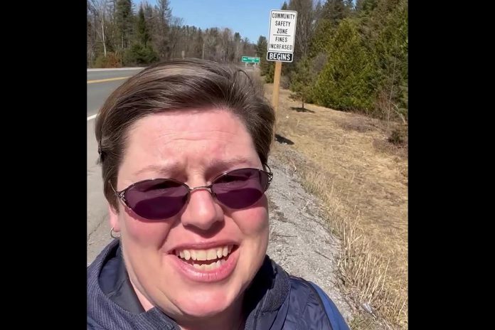 North Kawartha Carolyn Amyotte stands beside one of the signs indicating new "community safety zones" along Highway 28 where fines for certain driving infractions are doubled. One zone covers 3.5 kilometres of the highway as it passes through Apsley and the other zone covers 5.8 kilometres of the highway from Haultain through Woodview. (kawarthaNOW screenshot of Facebook video)