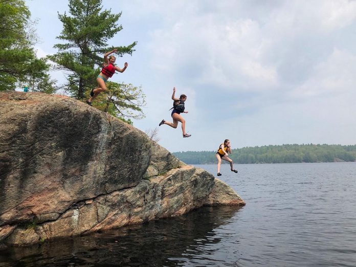 Based in Apsley in North Kawartha Township, The Land Canadian Adventures provides authentic experiences that immerse children and youth in nature while building their skills and their confidence in the outdoors by creating opportunities for supervised risk. Here, three Young Trippers leap off the cliffs in proven-safe spot at the end of a portage from Anstruther Lake to Rathbun Lake in Kawartha Lakes Highlands Provincial Park. (Photo courtesy of The Land Canadian Adventures)