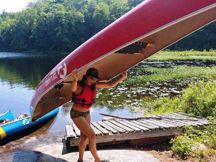 A Young Tripper shows off her muscle by hefting a canoe over her head for the 160 metre or so portage between Rathbun and North Rathbun Lakes in Kawartha Highlands Provincial Park.  (Photo courtesy of The Land Canadian Adventures)