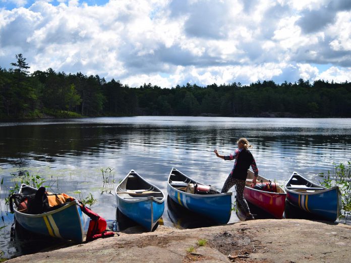 A Young Tripper dances around canoes pulled up on shore in Kawartha Highlands Provincial Park. Youth learn about self-reliance, teamwork, and determination in an environment of supervised risk.  (Photo courtesy of The Land Canadian Adventures)