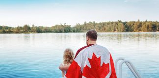 A man wrapped in the Canadian flag sitting on a dock with his young daughter. (Stock photo)