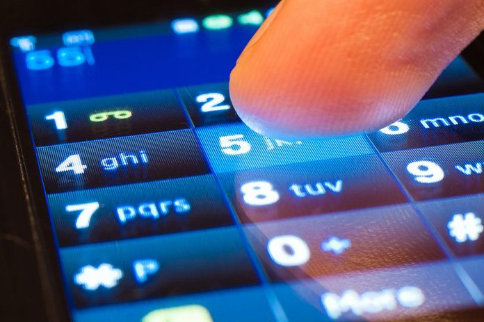 A finger dials a number on a smartphone's touchscreen. (Stock photo)