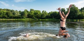 Two girls jumping off a dock into a lake during the summer. (Stock photo)