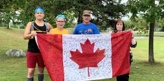 Runner Joel Kimmett (left), Eileen Kimmett, Clay Williams, and Julie Chatten (representing Peterborough-Kawartha MPP Dave Smith) at the Peterborough Lift Lock on August 23, 2022, the fourth day of the annual Canal Pursuit for Mental Health, a 700-kilmetre relay run from Port Severn to Ottawa. Williams began the run in 2015, which has since raised almost $100,000 for Mood Disorders Society of Canada, to raise awareness and end the stigma around mental health issues. The Canadian flag has been signed by hundreds of people Williams has met during the eight years of the run, including the first two years when he ran the entire route himself. (Photo courtesy of Eileen Kimmett)