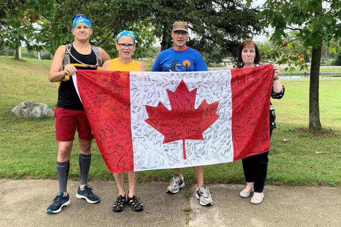 Runner Joel Kimmett (left), Eileen Kimmett, Clay Williams, and Julie Chatten (representing Peterborough-Kawartha MPP Dave Smith) at the Peterborough Lift Lock on August 23, 2022, the fourth day of the annual Canal Pursuit for Mental Health, a 700-kilmetre relay run from Port Severn to Ottawa. Williams began the run in 2015, which has since raised almost $100,000 for Mood Disorders Society of Canada, to raise awareness and end the stigma around mental health issues. The Canadian flag has been signed by hundreds of people Williams has met during the eight years of the run, including the first two years when he ran the entire route himself. (Photo courtesy of Eileen Kimmett)