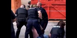 Peterborough police officers arrest Frank Curtin during a protest at the Peterborough police station on August 13, 2022. A follower of self-proclaimed "Queen of Canada" Romana Didulo, Curtin organized and led the protest to "arrest" Peterborough police officers after a call from Didulo, who espouses a mix of sovereign citizen beliefs, QAnon conspiracy theories, and new age spirituality. Didulo also claims to be an extraterrestrial being with supernatural powers. (kawarthaNOW screenshot of Twitter video)