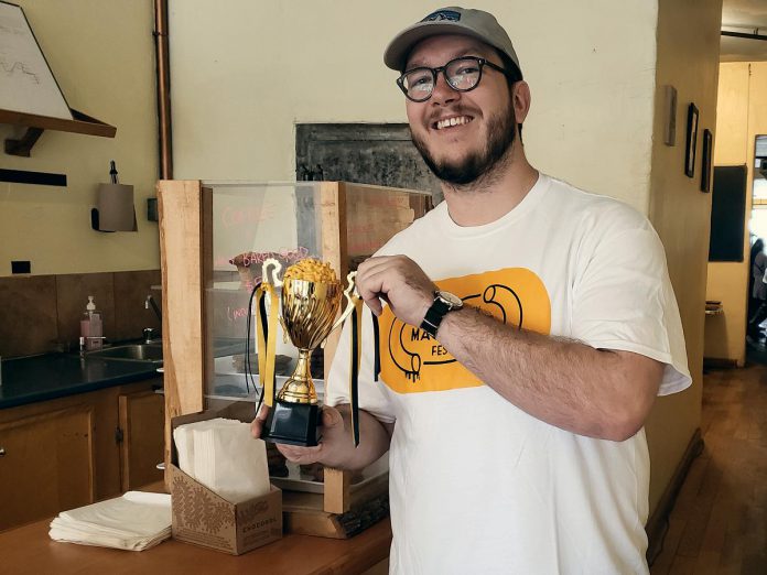 Owen Walsh of Sam's Place Deli displays the trophy the restaurant won during the 2021 Peterborough Mac + Cheese Festival for their Jalapeño Bacon Mac + Cheesewich, at the launch of the second annual  Peterborough Mac + Cheese Festival at The Food Shop on Water Street on September 28, 2022. (Photo: Jeannine Taylor / kawarthaNOW)