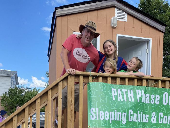 Peterborough teacher Aaron McFadden with his children at the prototype "tiny home" for people experiencing homelessness. McFadden will be sleeping in the cabin on Rubidge Street opposite Cathedral of St. Peter-in-Chains overnight on September 3, 2022 to raise awareness and funds for the Peterborough Action for Tiny Homes (PATH), a grassroots initiative with the goal of creating a village of 50 tiny homes to help house some of the 317 people without a home in Peterborough. (Photo courtesy of PATH)
