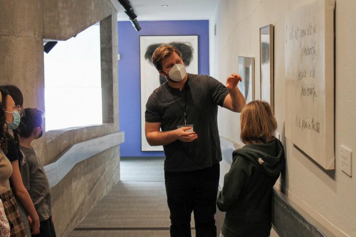 Andrew Ihamaki, Education Programming Coordinator at the Art Gallery of Peterborough, giving a gallery tour to local children. Through fundraising events like the "It's All About ART" auction and the support of other local businesses, the Art Gallery of Peterborough can continue to support and showcase the work of local artists and provide programming to the community. (Photo courtesy of the Art Gallery of Peterborough)