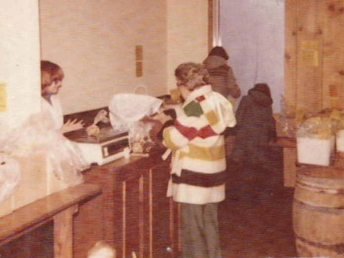 Deb Fraser serving a customer during The Main Ingredient bulk food store's first day of operation in 1979. The top of the couple's newborn son's head can be seen at the bottom of the photo.  (Photo: The Main Ingredient / Facebook)