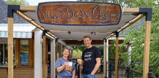 The Canadian Canoe Museum executive director Carolyn Hyslop and Silver Bean Cafe owner Dan Brandsma celebrate their new partnership by donning each other's t-shirts and raising a cup of coffee to their future together. The Silver Bean Café on the Lake will operate seven days a week at the new Canadian Canoe Museum at 2077 Ashburnham Drive on the shores of Little Lake when the new museum opens in summer 2023. (Photo courtesy of The Canadian Canoe Museum)