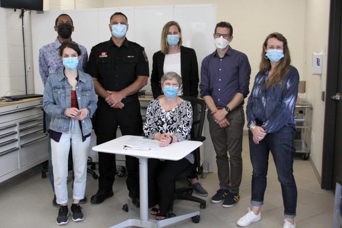 Dr. Thomas Piggott (second from right) representing Peterborough Public Health at a May 26, 2022 media tour of Peterborough's new Consumption and Treatment Services (CTS) site at 220 Simcoe Street in downtown Peterborough. Also pictured are other representatives of the CTS partner agencies: Safer Supply Program supervisor Carolyn King (front left), Fourcast executive director Donna Rogers (seated), Peterborough 360 Degree Nurse Practitioner-Led Clinic clinical director Kelly Pensom (front right) and (back row) PARN interim executive director Dane Record, Peterborough City-County Paramedics commander Craig Jones, and CTS program manager Kerri Kightley. (Photo: Jeannine Taylor / kawarthaNOW)