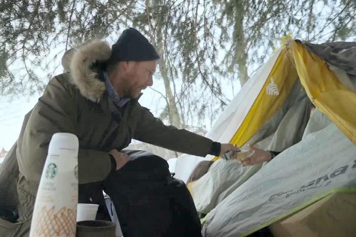 Chris Vyn, former outreach worker with One City Peterborough, provides food and supplies to a woman experiencing homelessness during a winter 2022 outreach program funded by the United Way of Peterborough & District for which funding ended last March. Vyn is volunteering at One City Peterborough's 'Everyone Belongs' event on November 30, 2022 at the Market Hall in downtown Peterborough, which intends to raise awareness about the work of the nonprofit charitable organization as well as funds. (kawarthaNOW screenshot of One City Peterborough video)