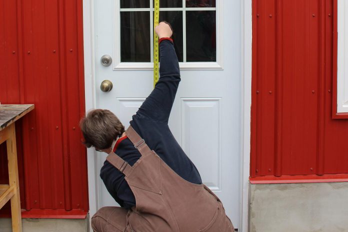 Reducing emissions through community action is important. GreenUP registered home energy advisor Clara Blakelock measures the height and width of a door as part of a home energy assessment. Her report will provide a homeowner with quantifiable data about the energy performance of their home and will inform the owner of strategies to reduce emissions.  (Photo: Lili Paradi / GreenUP)