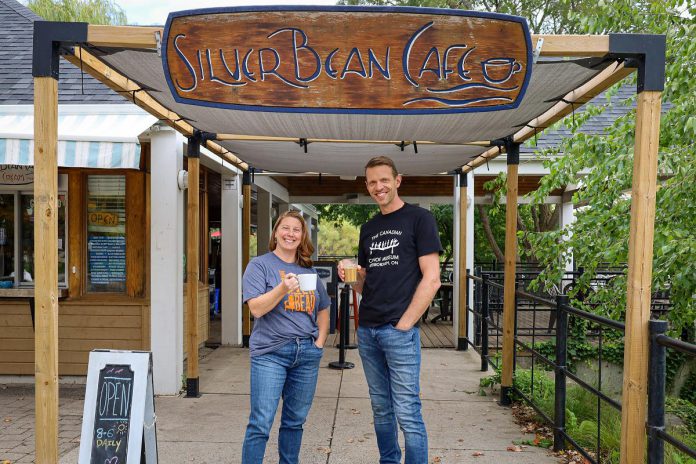 The Canadian Canoe Museum executive director Carolyn Hyslop and Silver Bean Cafe owner Dan Brandsma celebrate their new partnership by donning each other's t-shirts and raising a cup of coffee to their future together. (Photo courtesy of The Canadian Canoe Museum)