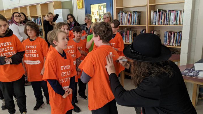 Hamilton-based musician, artist, and author Tom Wilson signs a student's "Every Child Matters" orange t-shirt during a December 8, 2022 event at Immaculate Conception Catholic Elementary School in Peterborough. (Photo: Bruce Head / kawarthaNOW)
