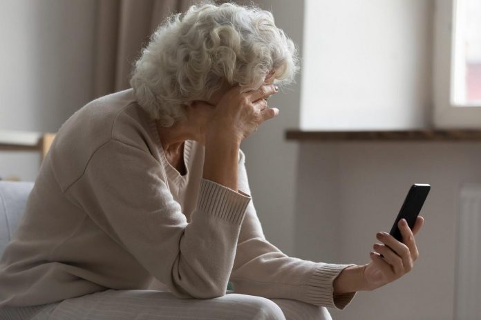 An older woman in distress looking at her mobile phone. (Stock photo)