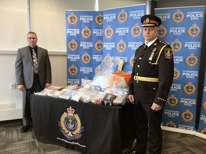 Peterborough police chief Stuart Betts (right) and detective staff sergeant Michael Jackson stand beside a table containing illicit drugs worth over $1.1-million that police seized after executing search warrants at several locations in Peterborough and at a Durham Region residence on January 25, 2023. A Peterborough man and women face multiple drug trafficking charges. (Photo: Peterborough Police Service)