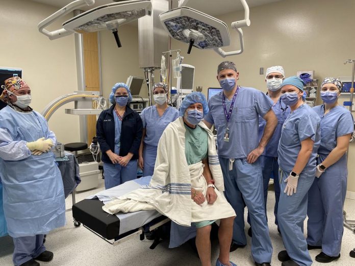 Patient Arthur Goard (seated) beside orthopaedic surgeon Dr. Sebastian Heaven at Ross Memorial Hospital in Lindsay on February 15, 2023 prior to the first Insignia femoral stem implant being used in hip arthroplasty surgery in Ontario. Also pictured from left to right: RPN Christine Ham, Registered Nurse First Assist Susan Dallas-Wood, RN Katie Oliver, anesthesiologist Dr. Mohammed Hussein, RN Michelle McCombe, and RN Kara Harman. (Photo courtesy of Ross Memorial Hospital)