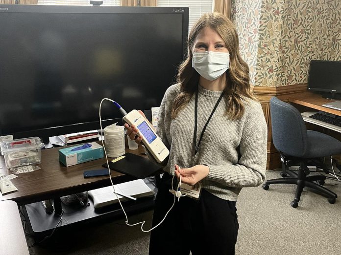 Five Counties staff member Lauren Richardson displays the device used to screen a newborn's hearing. The device measures the ear's (or brain's) response to soft sounds played to the baby. If needed, small stickers may also be placed on a baby's head. Infant hearing screening is safe, reliable and comfortable, and is generally best done when a baby is asleep. (Photo courtesy of Five Counties Children's Centre)