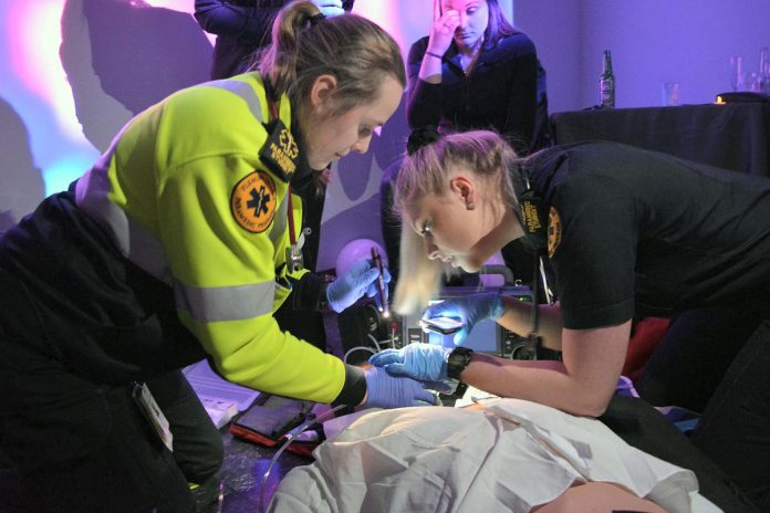 Paramedic students at Fleming College's on-campus simulation lab in 2019 participating in a simulation where a "groom" at a wedding (actually a high-fidelity manikin) was experiencing an anaphylactic response while surrounded by rowdy bystanders (played by graduates of the paramedic program). The students had to assess the groom and the scene to determine the appropriate treatment protocol. These scenarios help students prepare for real-world situations where they must act quickly under pressure. (Photo: Fleming College)