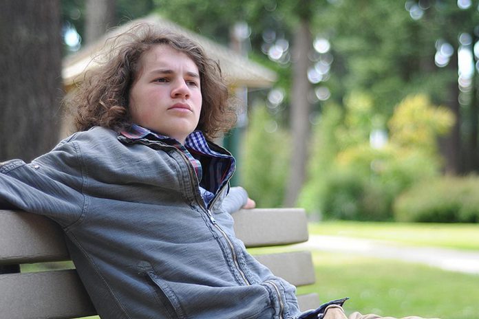 Teenage boy sitting on a park bench. (Stock photo)