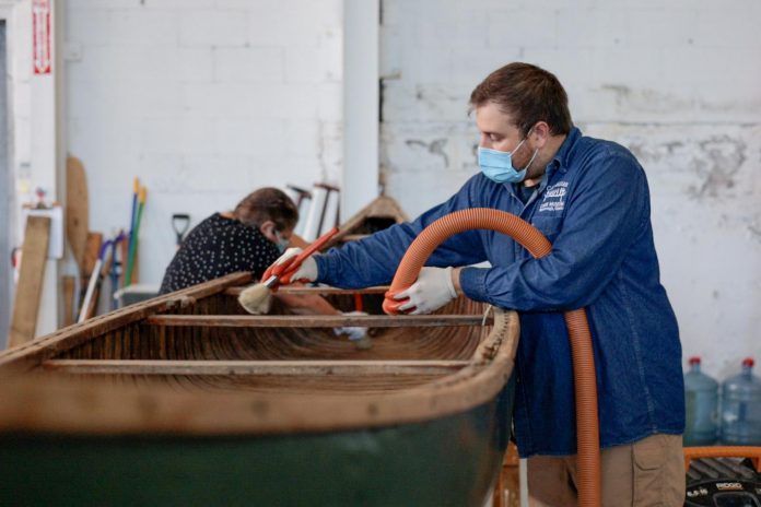 Two Canadian Canoe Museum staff members clean a canoe, with collections assistant Dane Allendorf using a brush and a vacuum, in preparation for the museum's move to its new home currently under construction at the water's edge on Little Lake in the heart of Peterborough. (Photo courtesy of The Canadian Canoe Museum)