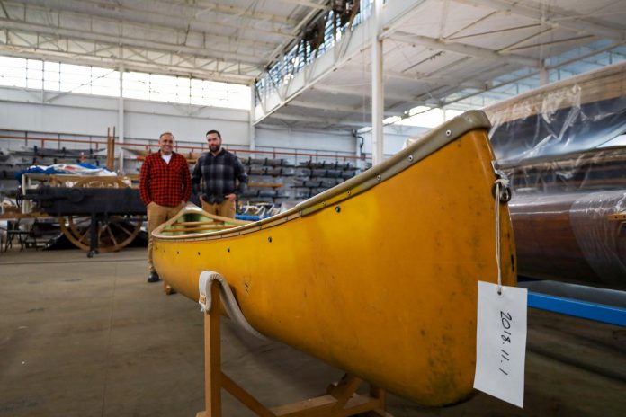 Neil Morton and Mike Judson, lead portagers for The Canadian Canoe Museum's "Move the Collection: The Final Portage" campaign, stand behind the late Gordon Lightfoot’s canary yellow canoe amidst the museum's collection, which is being prepared and packed in anticipation of the upcoming move to the museum's new waterfront home on the shores of Little Lake in Peterborough. (Photo courtesy of The Canadian Canoe Museum) 