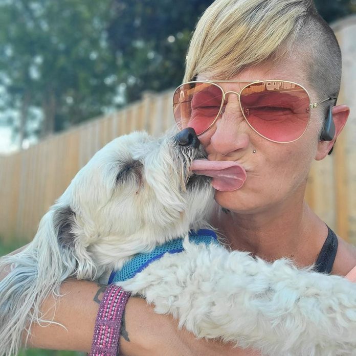 Meg Kynock gets a big kiss from muttmixx mascot Kevin Bacon. A full-time foster mom, Kynock had never baked before creating muttmixx, a healthy and natural treat that she says provides a variety of health benefits to dogs, including for Kevin after he almost lost his leg two years ago after being attacked by another dog and has now fully recovered. (Photo courtesy of Meg Kynock)
