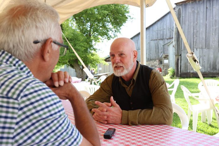 "The Cavan Blazers" actor JD 'Jack' Nicholsen (Patrick Maguire) speaks with kawarthaNOW writer Paul Rellinger during 4th Line Theatre's media day on June 14, 2023.  on July 19, 2023. The play, which chronicles the 19th-century conflict between Cavan Township's Protestant and Catholic Irish settlers, runs Tuesdays to Saturdays from August 1 to 26 at the Winslow Farm in Millbrook. (Photo: Heather Doughty / kawarthaNOW)