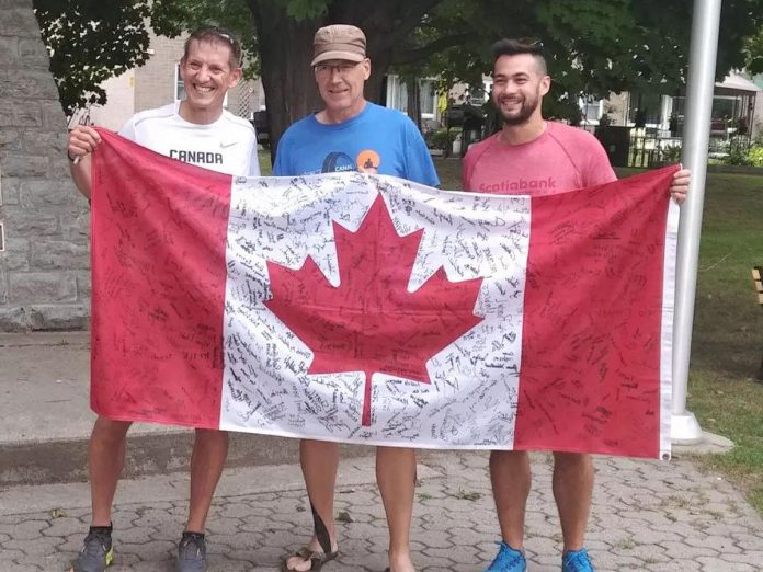 Canal Pursuit For Mental Health founder Clay Williams (middle) in Ottawa during the 2022 relay run that raises funds and awareness for mental health. For the 9th annual event, which takes place from August 19 to 26, 2023, Williams will once again carry the Canadian flag that each year is signed by people who have or know someone with mental health issues. (Photo: Canal Pursuit For Mental Health)