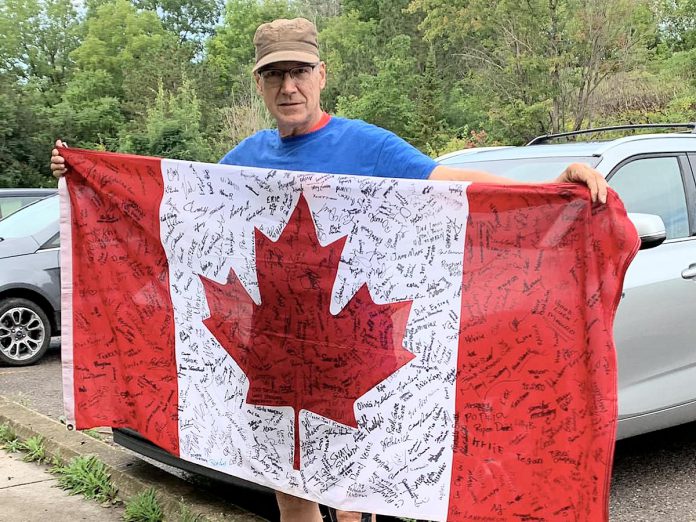 Canal Pursuit For Mental Health founder Clay Williams holds the Canadian flag that serves as a baton for the relay run. For eight years, he's asked people along the route to sign the flag if they or someone they know has mental health issues. It now has around 400 signatures. (Photo: Eileen Kimmett)