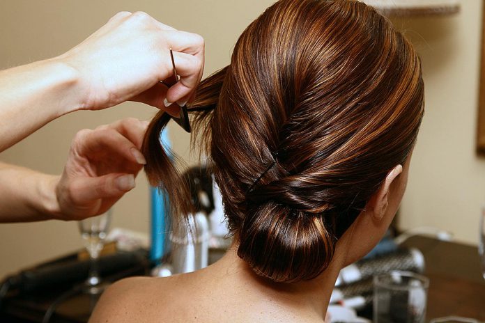 A hair stylist works on a woman's hair. (Stock photo)