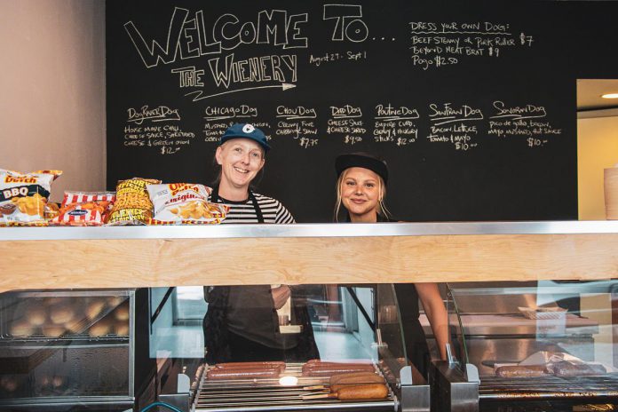 Sam Sayer (left), owner of downtown Peterborough's Sam's Place Deli, has soft launched a new wienery located directly behind the deli at 188 Hunter Street, serving up beef, pork, vegetarian hot dogs that can be purchased plain or loaded in classic and one-of-a-kind styles. (Photo: Peterborough Downtown Business Improvement Area)