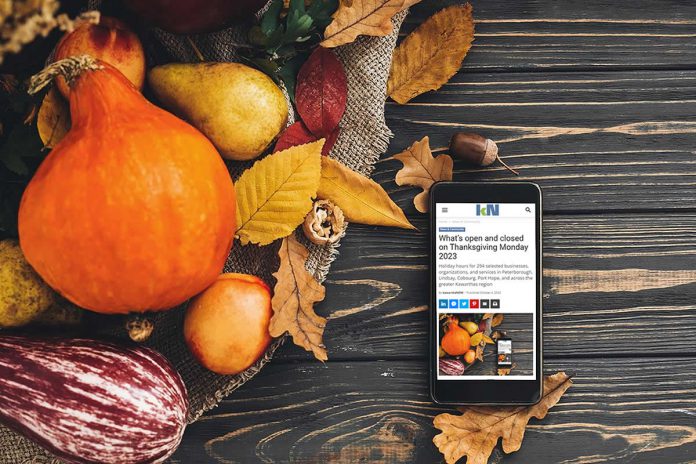 A mobile phone sitting on a harvest table covered with squash and fall leaves displaying kawarthaNOW's Thanksgiving Monday 2023 holiday hours story. (kawarthaNOW photo)