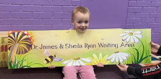 Maisie, one of the 6,200 children and youth served by Five Counties Children's Centre in the past year, helps display a sign the charitable organization serving children with special needs in the greater Kawarthas region will hang in the waiting area of its Peterborough location in recognition of a $227,000 donation from retired Peterborough couple James and Sheila Ryan to help reduce wait times. (Photo courtesy of Five Counties Children's Centre)